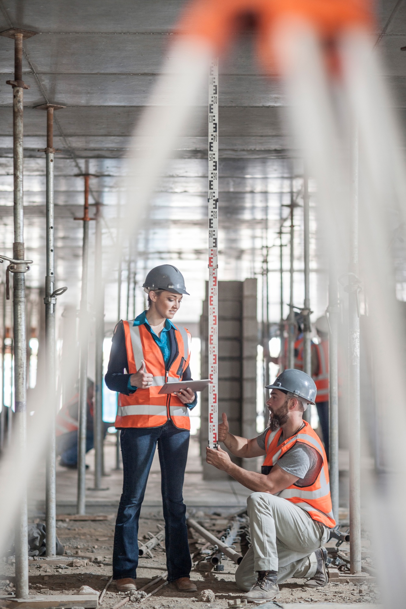 Male and female builders measuring construction with ruler